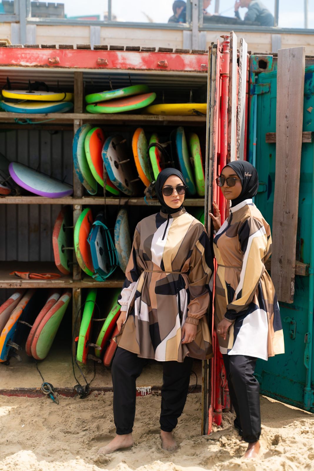 Two women posing in front of a rack of colourful surfboards