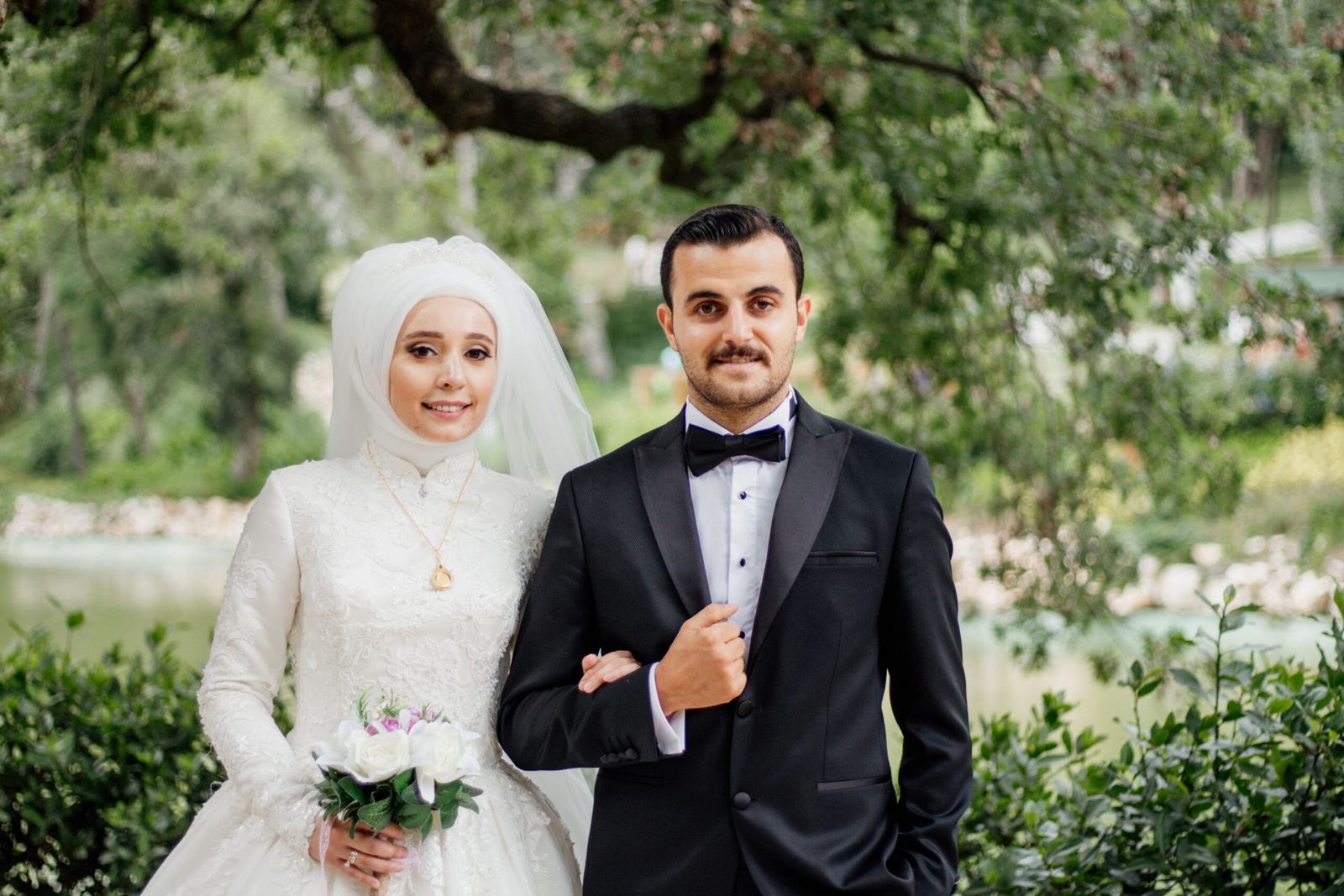 Bride in a white hijab and groom in a tuxedo in a garden