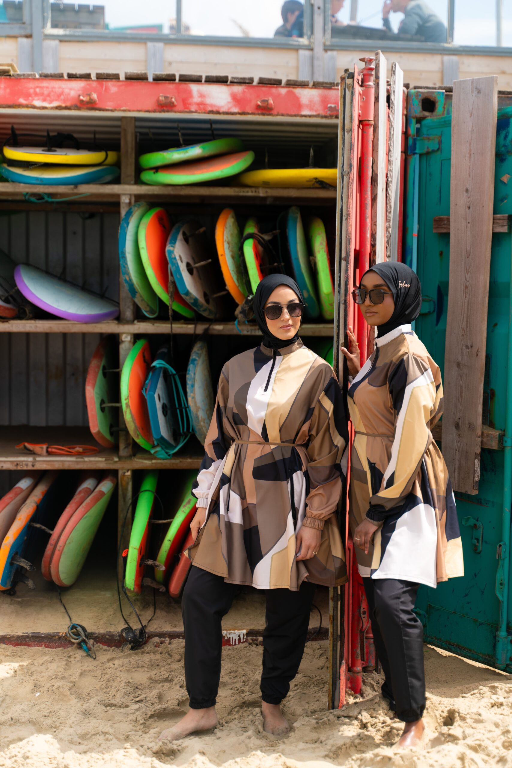 Two women posing in front of a rack of colourful surfboards