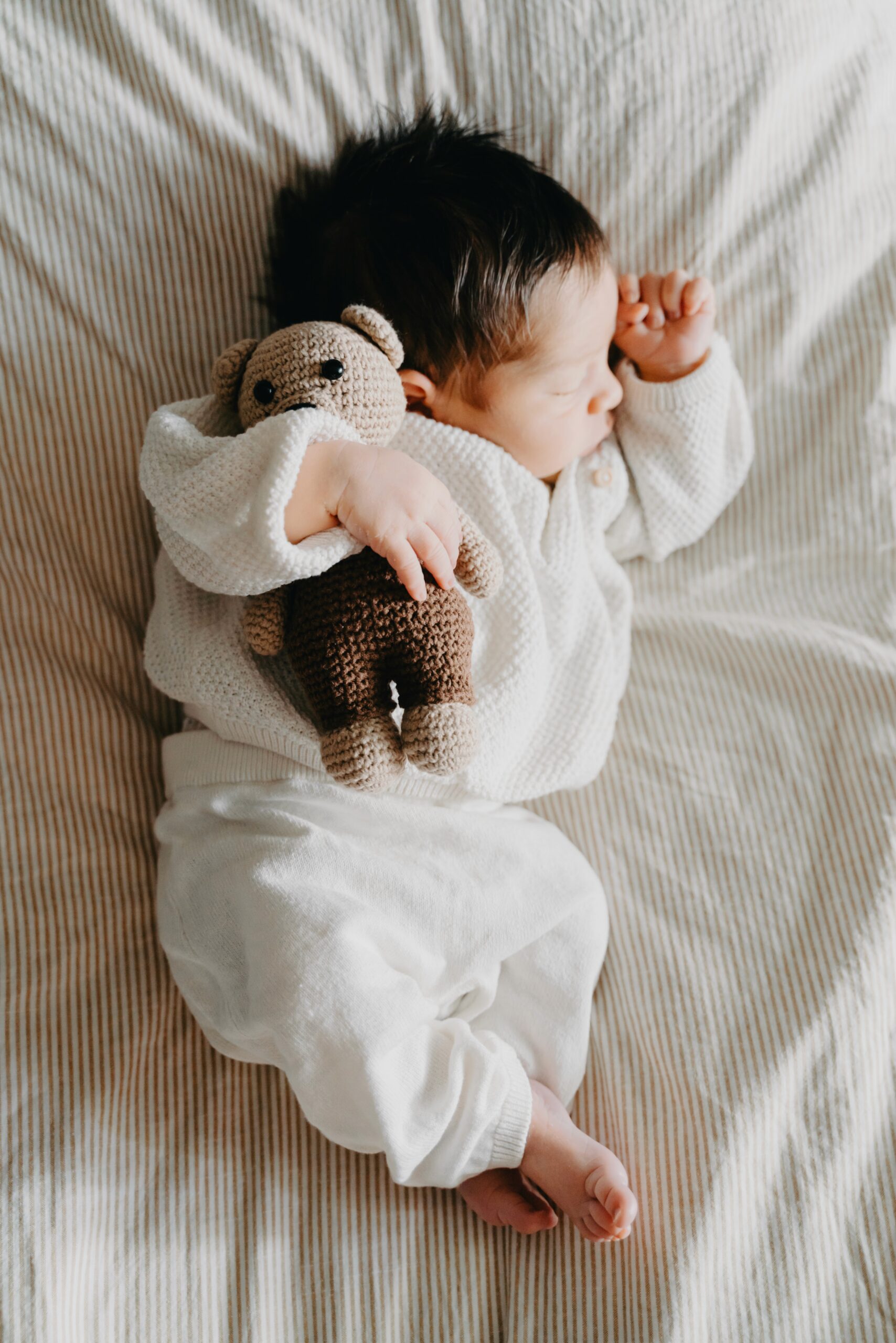 Newborn baby sleeping in a white outfit, seen from above