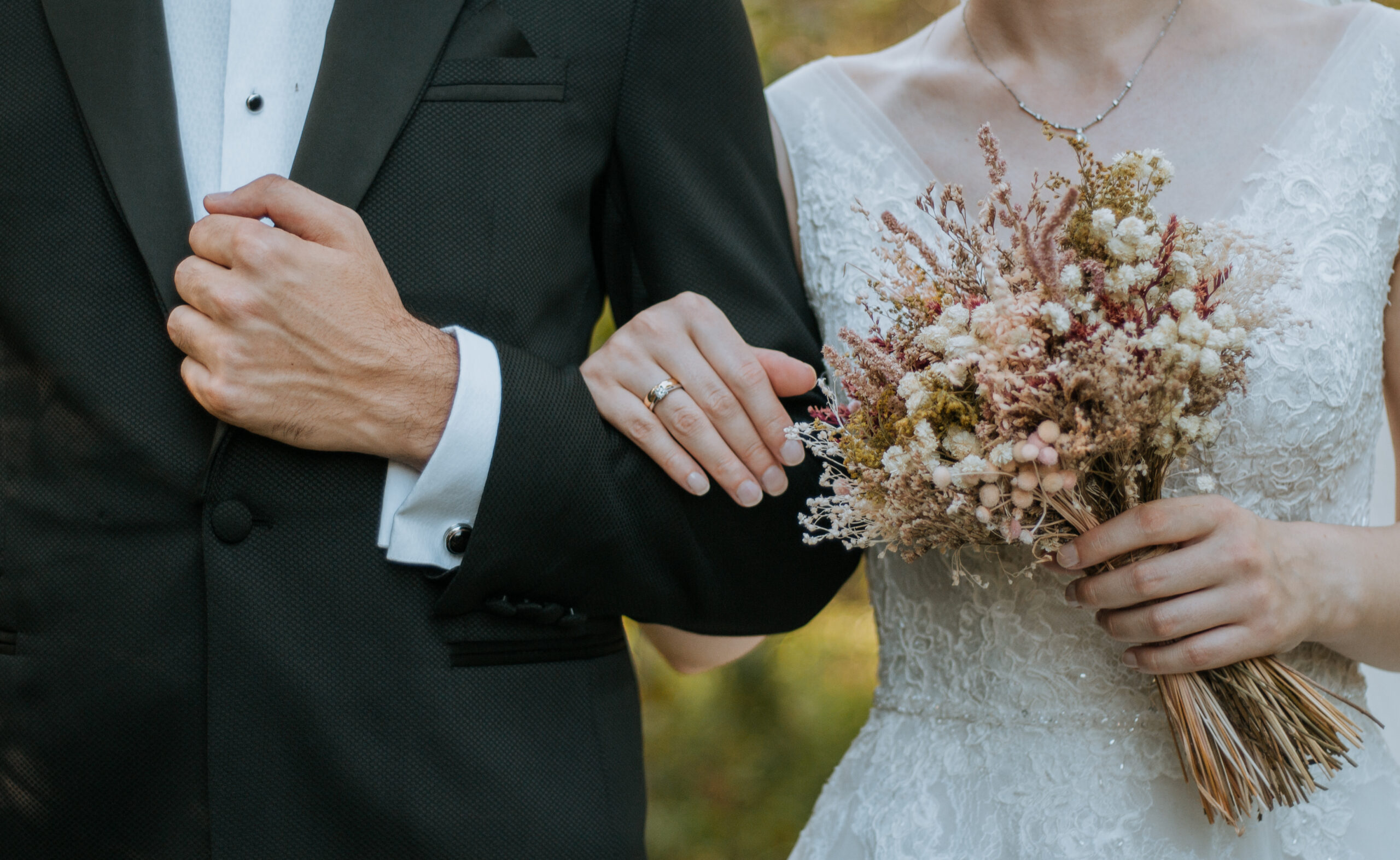Groom in a tuxedo beside the bride holding a dried-flower bouquet