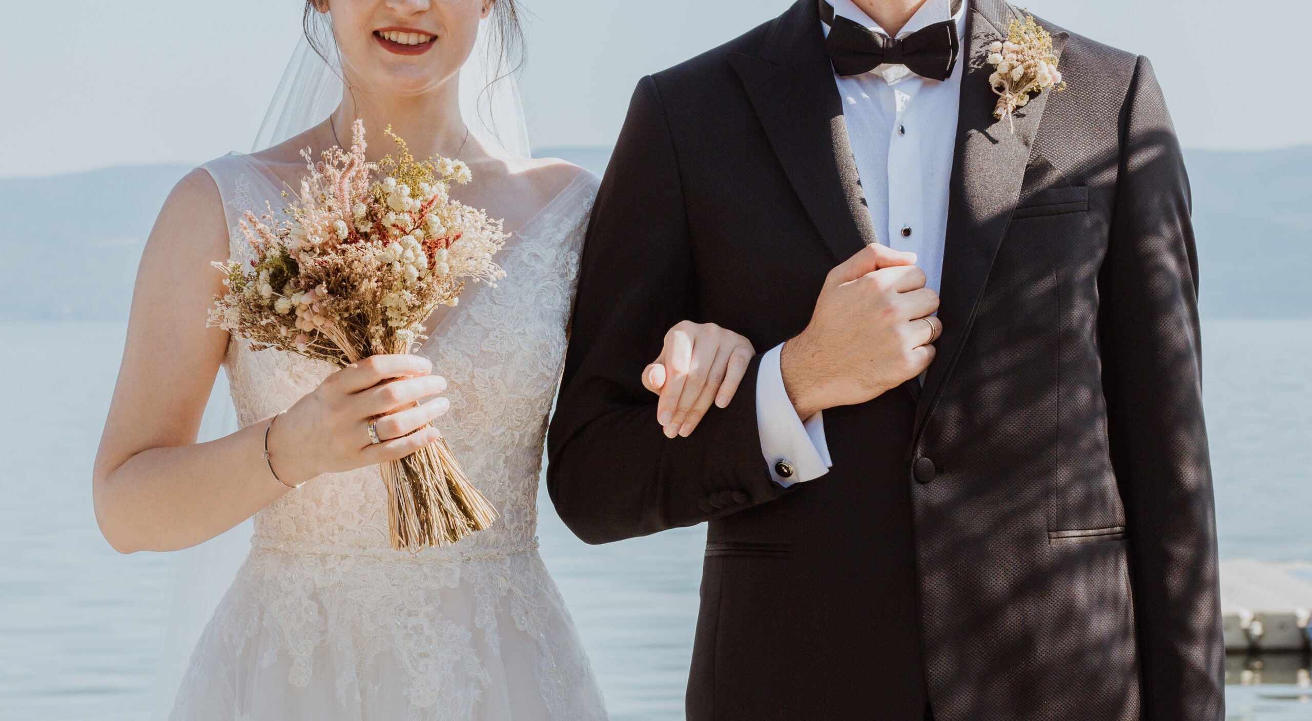 Bride with a bouquet and groom in a tuxedo by the sea
